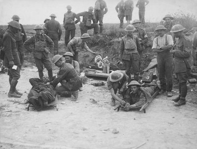 a black and white photograph of French soldiers tending to wounded battlem Richmond lines, WWI. In the background, other British troops stand in formation on an open field with a small wooden platform at their feet. On top of that platform lies one british soldier who is being displayed by another uniformed man wearing his helmet and holding up some kind of emblem or object for people around him to see. There's also several scattered bodies lying down nearby. This scene was captured during World War I. It was shot using Kodak film.