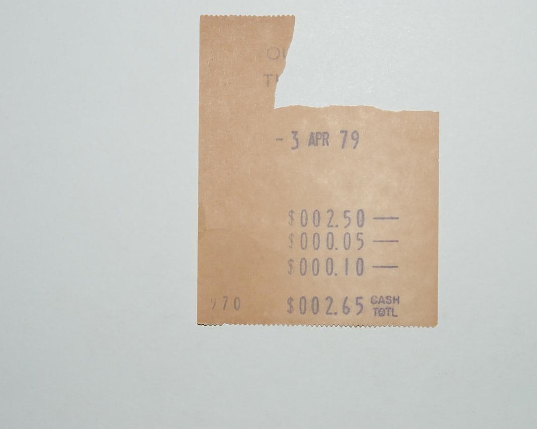 A small, crumpled beige cash register paper with the date “3 perennial apr’79” at top and numbers showing money amount in middle on white background. The title is “Six tight shops”, a line of text under it reads” $025 CASHConnor T uno’s”. There’s an inscription “Azgrul O Robbie” on bottom right corner. . A photo taken by canon eos r6, wide angle lens,