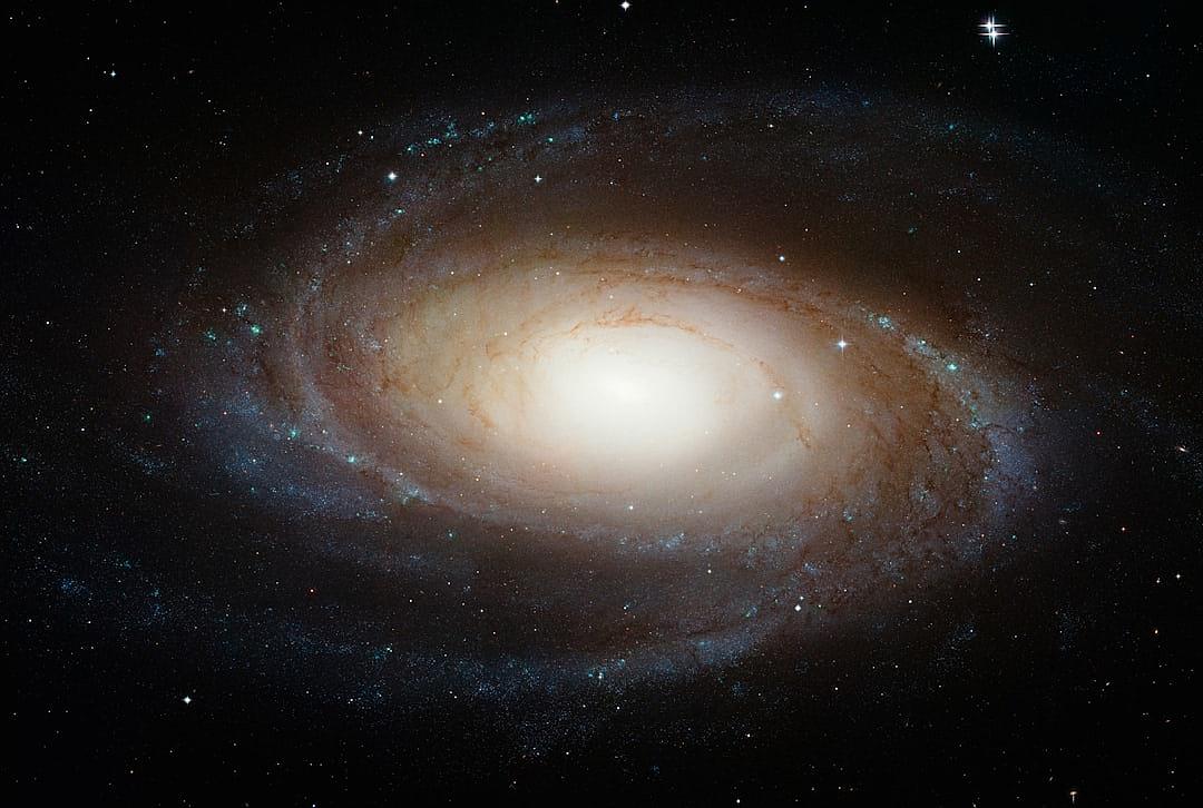 A spiral galaxy with the bright center of its core glowing, set against black space, with stars scattered around it. The Milky Way is visible in the background.