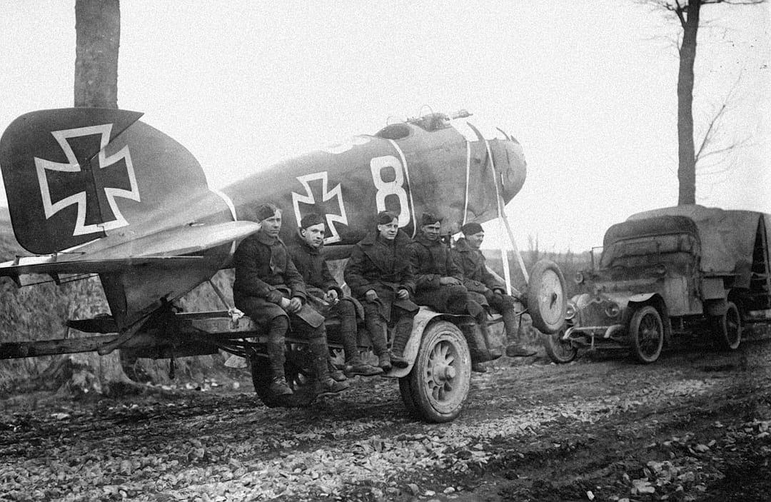 german soldiers sitting on the wing of an al – ultra one plane, painted with white “8” and black cross, near by is parked old truck with large gun, late autumn day in western germany, 20th century photo from camera obscura