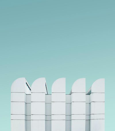 A minimalist composition featuring five white structures with rounded edges, arranged in an orderly fashion against the backdrop of a light blue sky. The composition is designed to create a sense of symmetry and balance between these geometric shapes, emphasizing their clean lines and simplicity. This image has been captured using a Sony Alpha A7 III camera for its high resolution and sharpness. The style of the image is reminiscent of minimalist works.