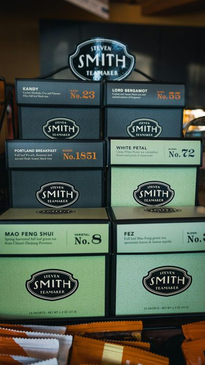 A display of tea boxes with the name "Steamer Smith" on them, each box featuring different types and packaging styles for black green white or purple Blackboard style Tea brand logo is displayed above with its unique label " no . No.23 P Celtic pattern , 54906", " portland breakfast". The words under it say "No.8." below that says "MAO FEN SHU evaluates white petal teal and spearmint leef my童装en." There's also an ad which reads " steamer smith s'more from Xinglong mountain in Shenzhen city," as well as