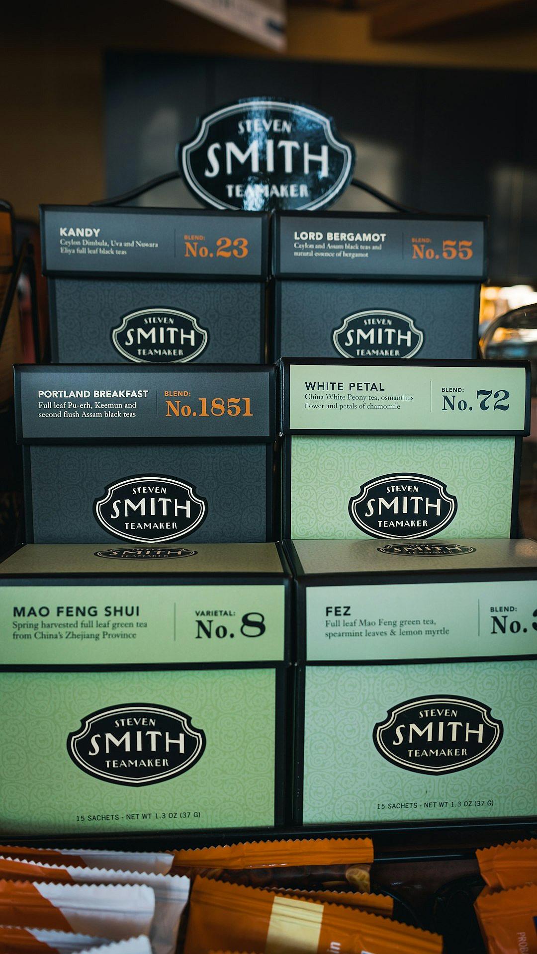 A display of tea boxes with the name “Steamer Smith” on them, each box featuring different types and packaging styles for black green white or purple Blackboard style Tea brand logo is displayed above with its unique label ” no . No.23 P Celtic pattern , 54906″, ” portland breakfast”. The words under it say “No.8.” below that says “MAO FEN SHU evaluates white petal teal and spearmint leef my童装en.” There’s also an ad which reads ” steamer smith s’more from Xinglong mountain in Shenzhen city,” as well as