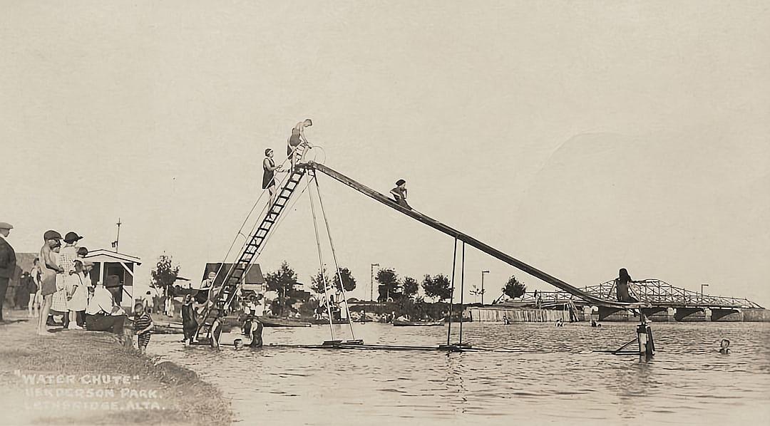 vintage photo of kids on a large water slide at “Wander Park” at the city’s lake, with people standing around watching, in the style of late Victorian era cabinet card, early American photography, vintage typography that says “Water Chute”, kids playing and laughing on the 50 foot tall slide, a bridge in the background.