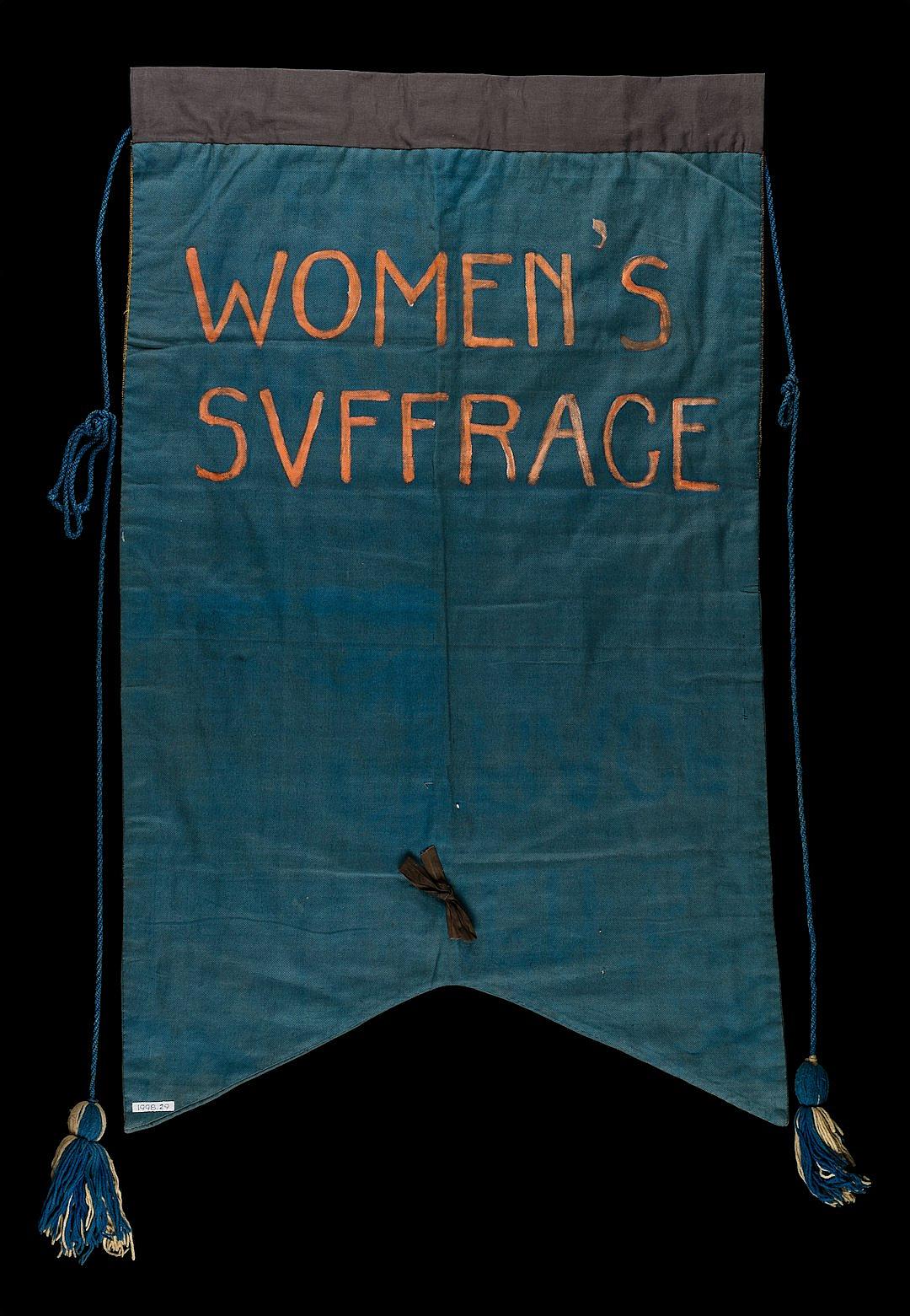 a banner with the words “WOMEN’Sglyph suff bureaucratsce” embroidered on it, blue fabric with dark tassels at each corner