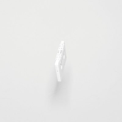 A white cassette tape floating in the air, on a white background. The cassette is a simple shape with clear edges and visible grooves along its surface. It has no text or graphics on it. There is nothing else around except for the solid color of light grey that makes up both the ground and sky. This simplicity highlights the object as being central to the composition, while also creating space between it and any potential surroundings.