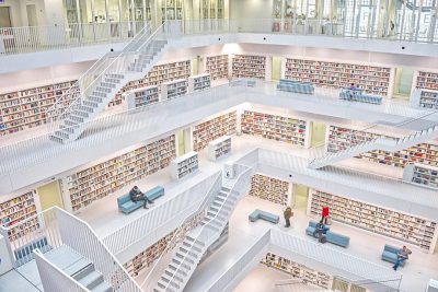 A white library with many books and stairs, people sitting on blue sofas in the center of each floor, wide angle view from above, hyper realistic photography in the style of bird's eye view.