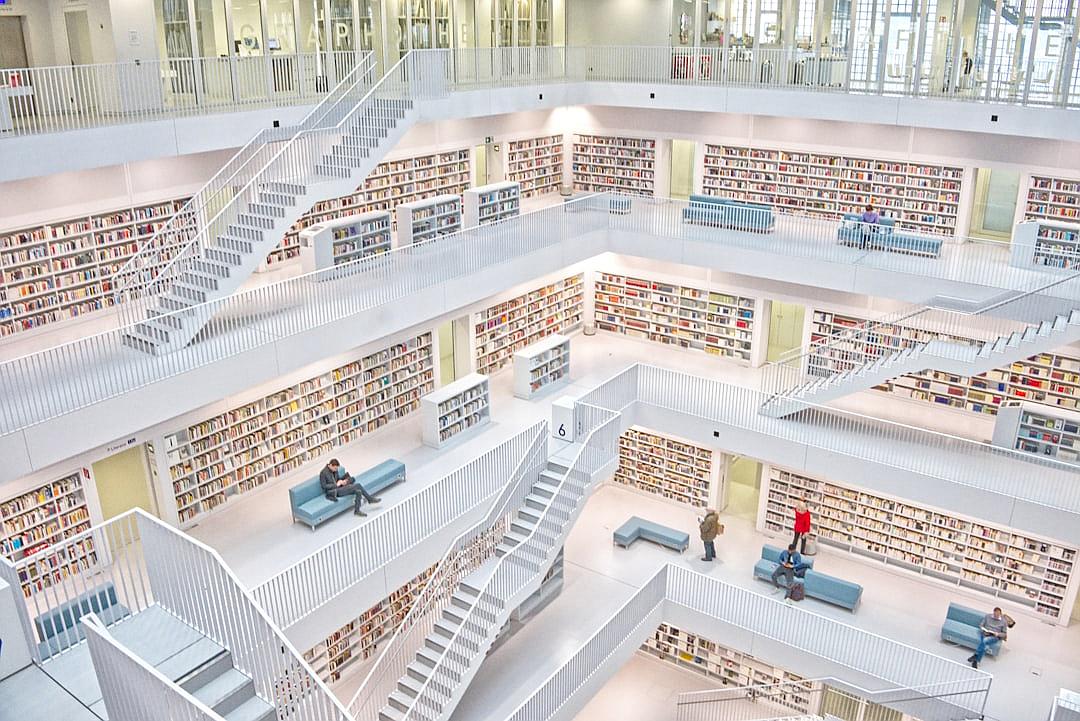 A white library with many books and stairs, people sitting on blue sofas in the center of each floor, wide angle view from above, hyper realistic photography in the style of bird’s eye view.