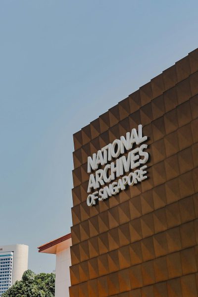 A large building with the words "national archive of singapore" on it, an architectural photography in the style of [Ross Lovegrove](https://goo.gl/search?artist%20Ross%20Lovegrove), minimalistic design, flat texture surface, made from bronze metallic material, logo for National Carlo Gold style architecture in Singapore, modern and sleek, background is clean sky, depth of field, high resolution, captured using Canon EOS R5 camera with Canon EF lens.