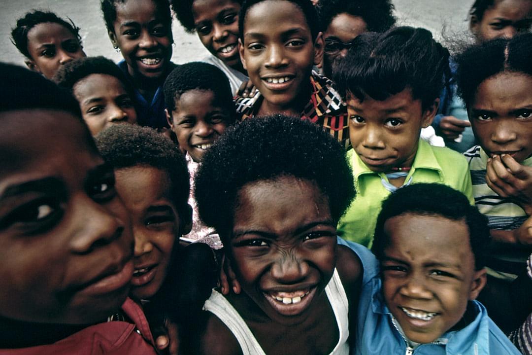 A group of happy black children in the style of [Martin Parr](https://goo.gl/search?artist%20Martin%20Parr), smiling at the camera, 1970s, retrofuturism, color photo in the style of [Henri Cartier-Bresson](https://goo.gl/search?artist%20Henri%20Cartier-Bresson)