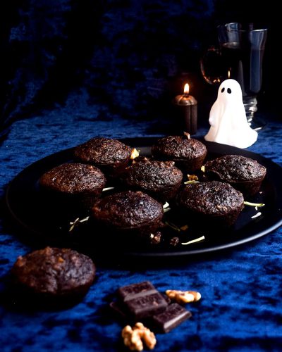 A plate of dark chocolate and walnut muffins, with a spooky Halloween theme and ghost shaped candles on the table, on a blue velvet cloth, in the style of food photography.