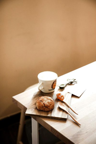 A photo of an empty table with a coffee mug, scones and cutlery on top, beige wall in the background, minimalist, taken in the style of Canon EOS R5.