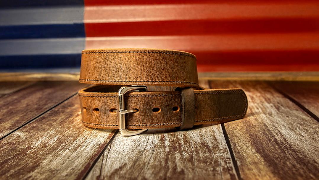 A brown leather power belt with a silver buckle on a wooden table, with an American flag in the background, in the style of product photography.