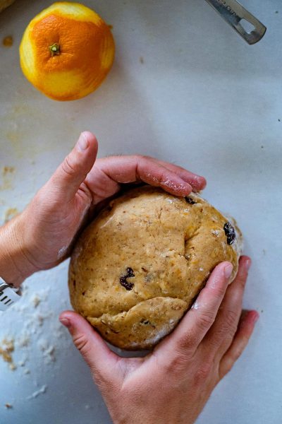 A photo of hands holding dough for orange z (!!fieldthis BUTTON fit! ze fabric stuffed oval bread with oranges and dark raisins, white background, top view, taken by Sony Alpha A7 IV