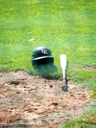 A baseball bat and helmet on the ground in front of home plate, with green grass behind it. The scene is captured from an angle that highlights details like dirt underneatth her head and small stones scattered around. This photograph was taken during daylight, using natural light to highlight textures and colors. It's in high resolution and has a resolution of 20 megapixels. In short, it creates a vivid representation of a typical game day at valley field