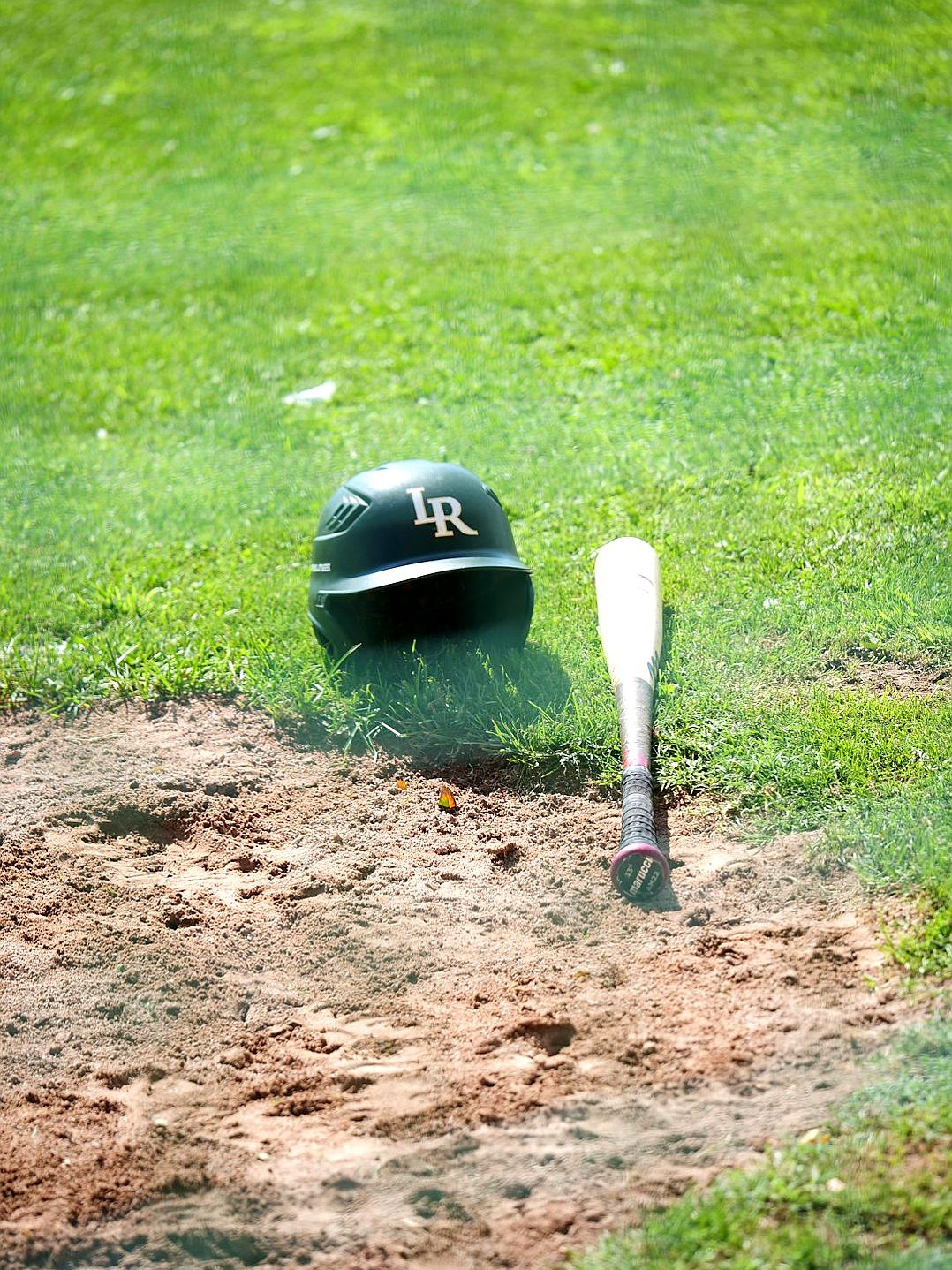 A baseball bat and helmet on the ground in front of home plate, with green grass behind it. The scene is captured from an angle that highlights details like dirt underneatth her head and small stones scattered around. This photograph was taken during daylight, using natural light to highlight textures and colors. It’s in high resolution and has a resolution of 20 megapixels. In short, it creates a vivid representation of a typical game day at valley field