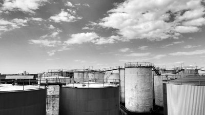 Black and white photo of industrial tanks in an oil production facility, wide angle, sky with clouds in the background, lowangle shot, Sony Alpha A7 III, Leica M6, f/8, 35mm lens,