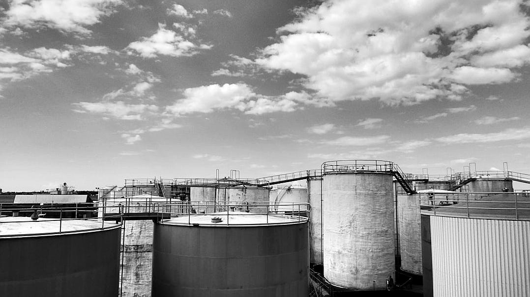 Black and white photo of industrial tanks in an oil production facility, wide angle, sky with clouds in the background, lowangle shot, Sony Alpha A7 III, Leica M6, f/8, 35mm lens,