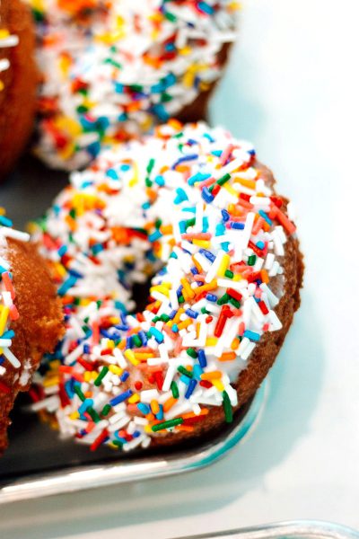 Close up photo of colorful sprinkled donuts on a glass plate against a white background, in the style of food photography by David Newton and in the style of Brownie Shumate, stock photo, flat lighting, bright.