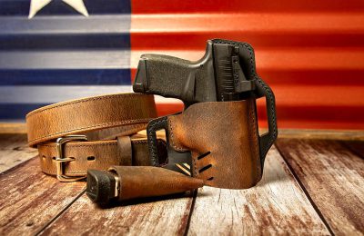 a gun in an brown leather holster with belt on the table, Texas flag background, product photography