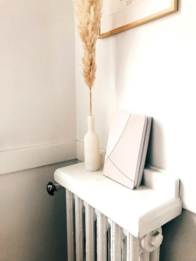 A white modern minimalist shelf with an open book and pampas grass next to it, on top of the radiators in the corner of a room, in the style of instagram aesthetic.