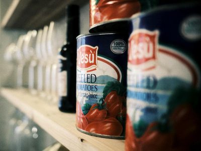 A close-up shot of the "Yesu" brand tomato sauce can standing on an empty shelf in front of other cans and bottles. The focus is sharp, highlighting intricate details like reflections or shadows that create depth. In soft light, the colors of tomatoes appear vivid against the blue label, emphasizing their natural beauty. This scene captures the essence of everyday life, showcasing simplicity while conveying freshness through visual elements in the style of a minimalist painter.