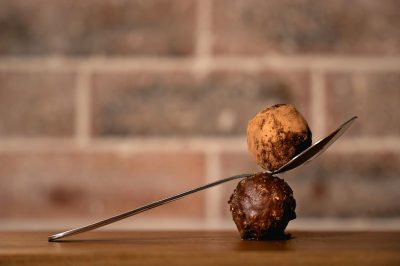 A spoon with truffle on it is balancing between two balls of chocolate, a background brick wall, Canon R5