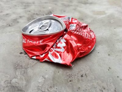 A photo of an empty and crumpled red "CocaCola" can, laying on the concrete floor in the style of [Banksy](https://goo.gl/search?artist%20Banksy).