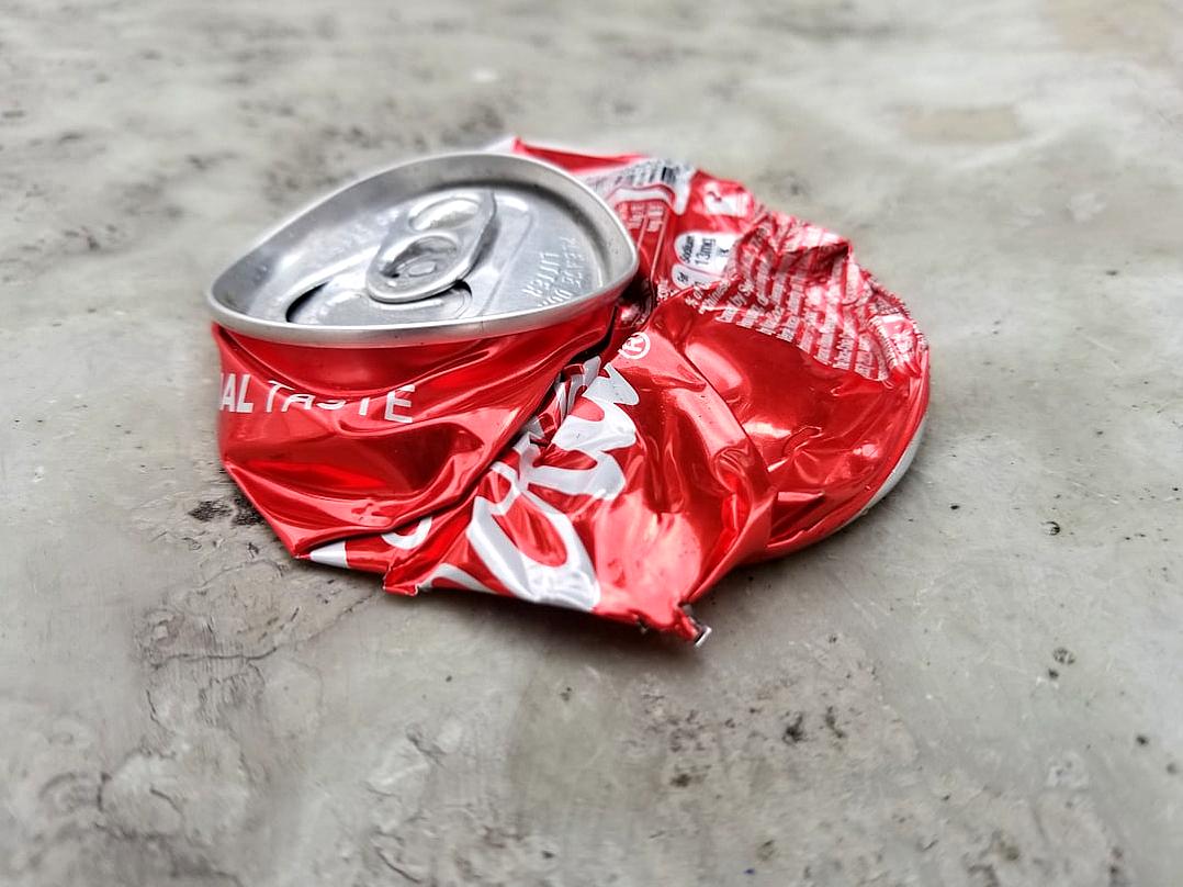 A photo of an empty and crumpled red “CocaCola” can, laying on the concrete floor in the style of [Banksy](https://goo.gl/search?artist%20Banksy).