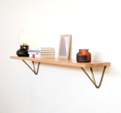 simple shelf with metal legs, light wood, and brass accents for a wall shelf, with books and photo frames on top of it, on a white background, in the style of product photography