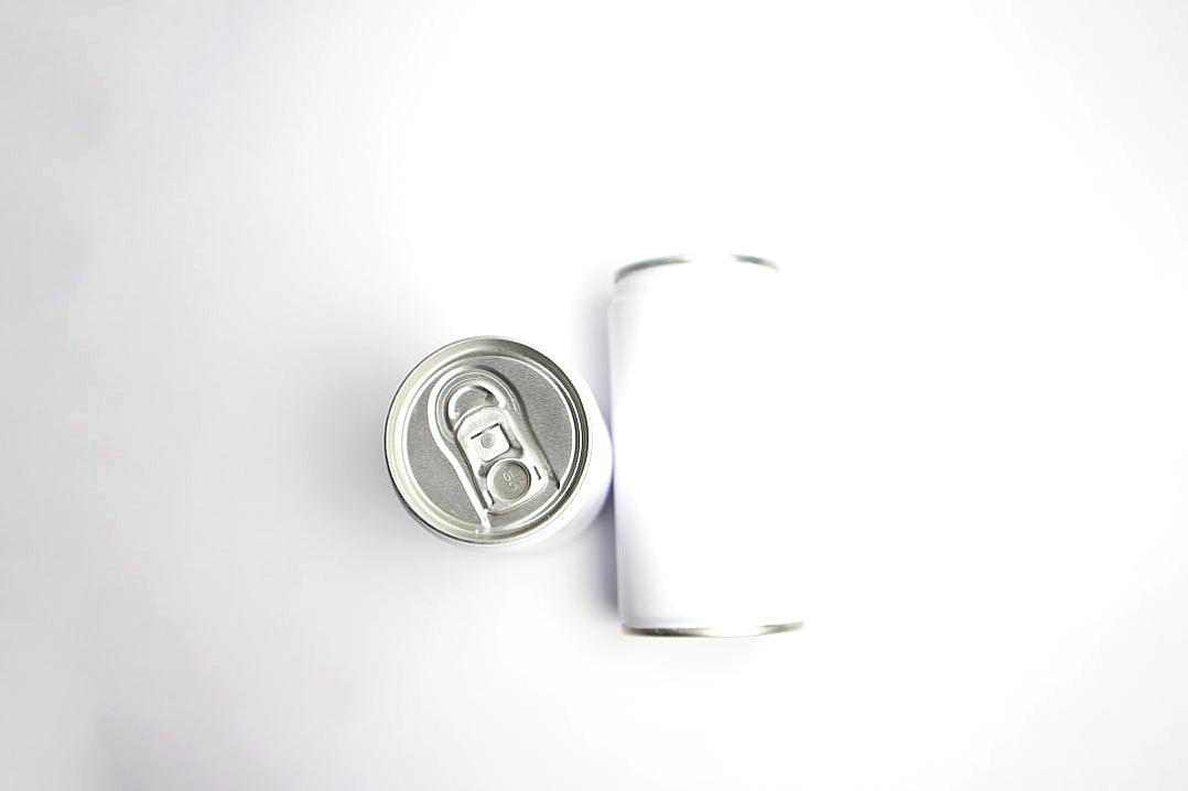 A blank white can of energy drink sits next to it on the table in a top view, captured through high resolution photography against a minimalist white background in the style of high quality, high definition photo.