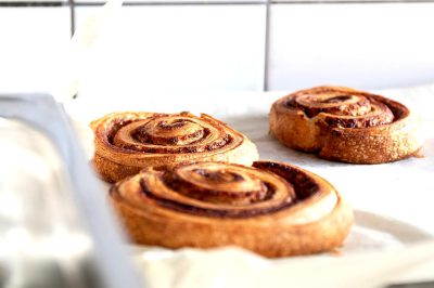 Caperlsen Buns, cinnamon rolls in an oven tray on a white kitchen counter, focusing on the spiral of the rolls in a harmonious composition in the style of Ci. High resolution food photography showing detailed texture and product shot closeups.