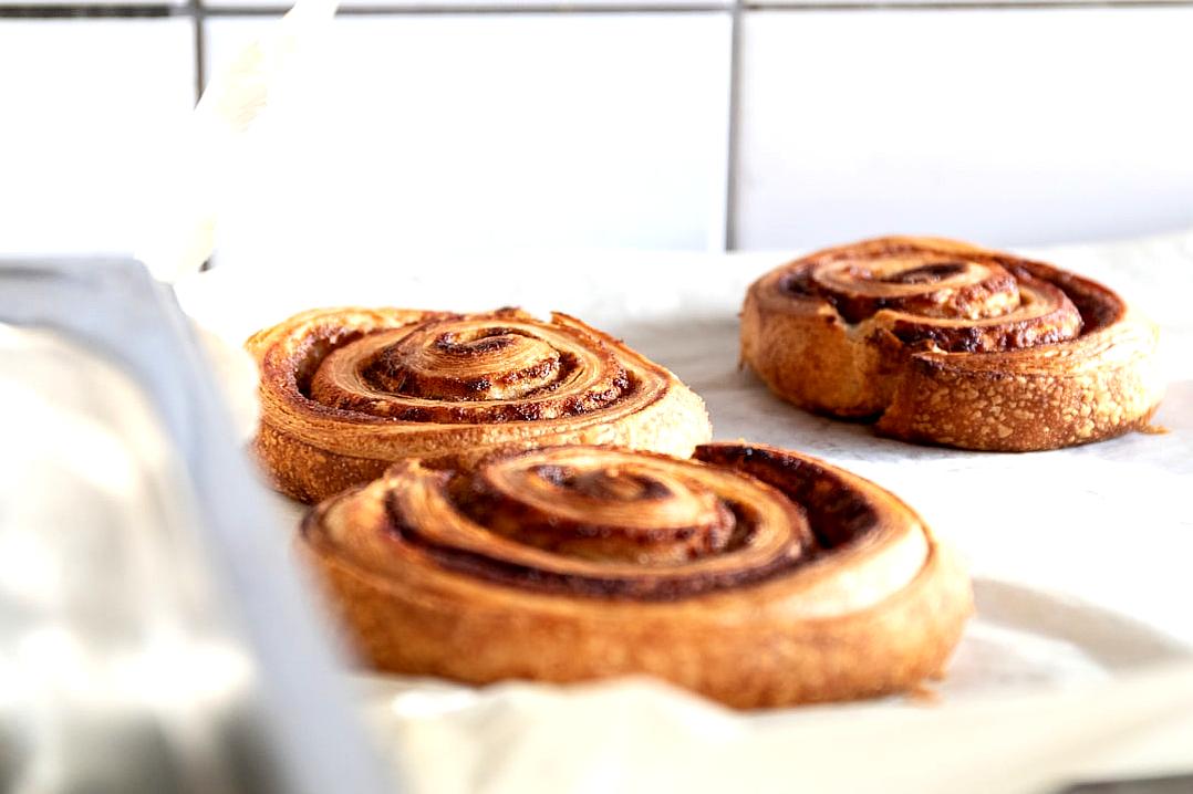 Caperlsen Buns, cinnamon rolls in an oven tray on a white kitchen counter, focusing on the spiral of the rolls in a harmonious composition in the style of Ci. High resolution food photography showing detailed texture and product shot closeups.