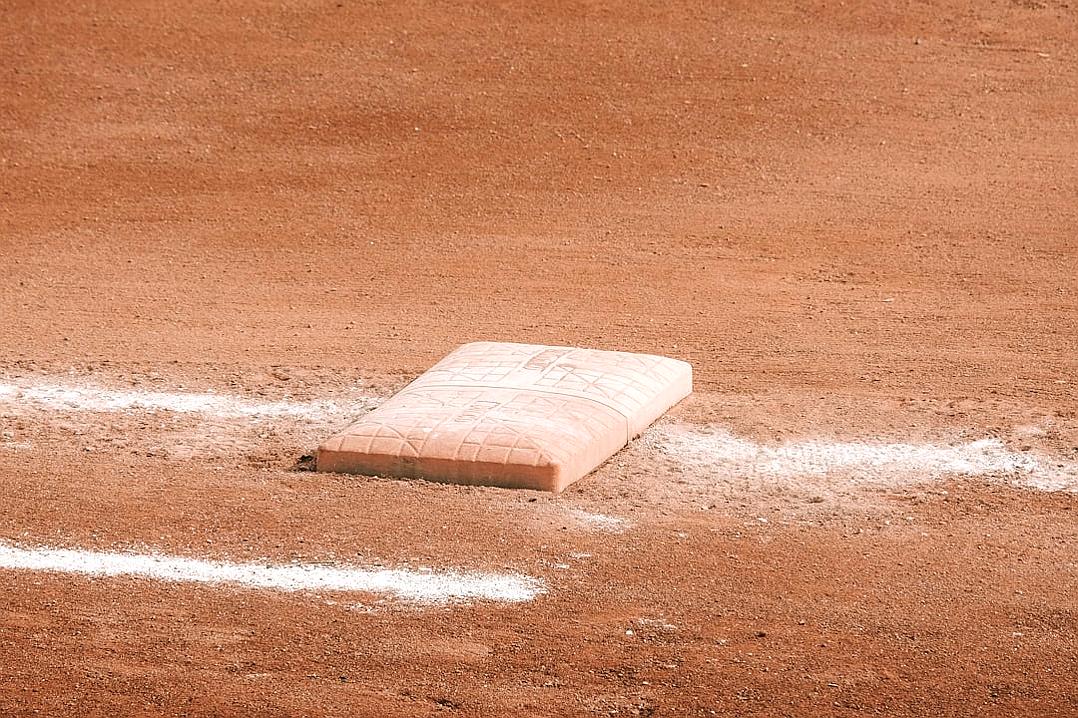 A flat, rectangular base at home plate on the field of an American baseball game. The background is a solid red dirt with white lines indicating first and second base boxes. There should be no people or equipment in frame to focus attention directly on the ground where you can see part of one bag of empty small clay pots lying next to it. The style resembles that of an unknown artist.