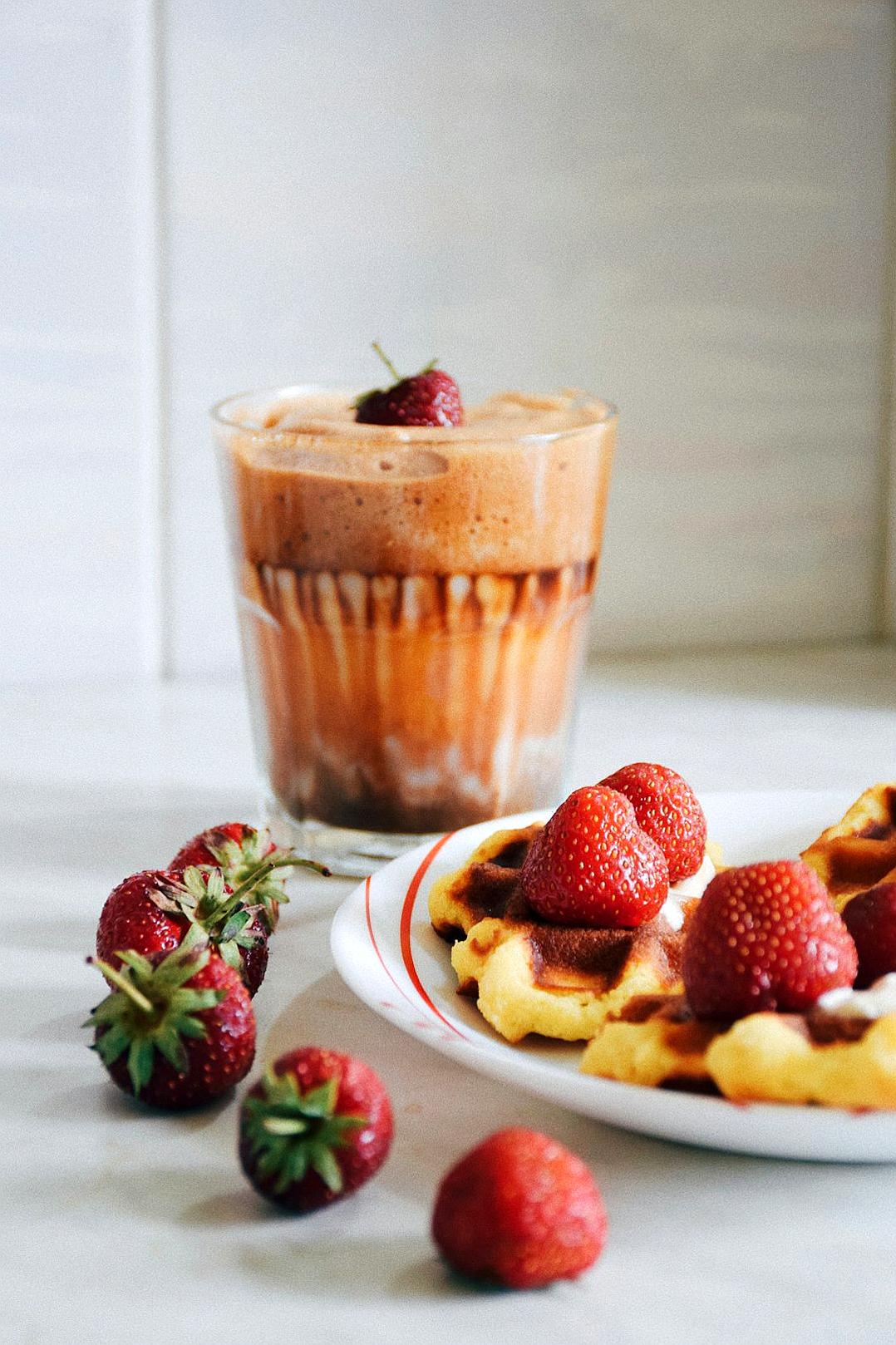 A photo of an ice latte in a glass with strawberries and waffles on the side, on a white table, food photography, food styling, minimalist, white background, in the style of minimalist.