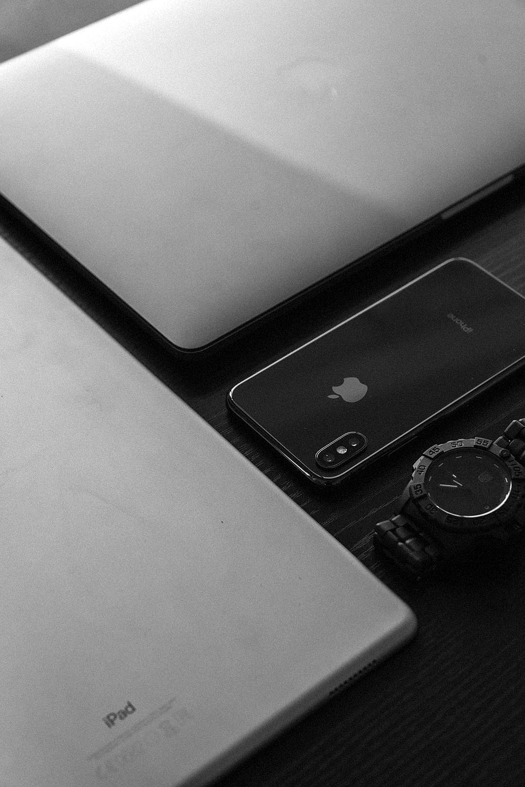 Black and white photography of an iPhone, macbook laptop and watch on the desk in the style of.