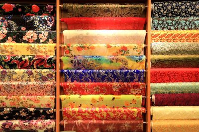 A colorful display of various fabrics in an Asian fabric store, including silk and cotton cloth with floral patterns. The fabric is arranged on shelves or stands to show their texture and coloration. This scene could represent the variety of textile colors and textures found at such stores, providing designers and artists material for creative expression in fashion design and art creation.