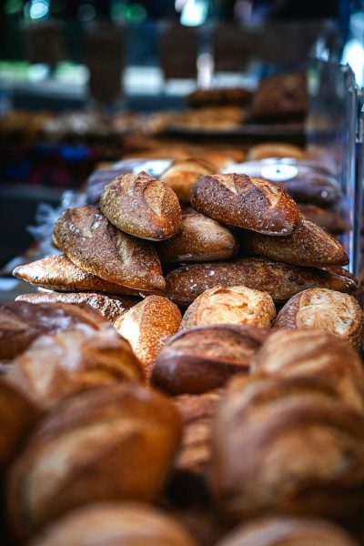 A closeup of the delicious loaves and baguettes at Lachlan's Easter bread stand, highlighting their golden brown crusts and soft textures, with other pastries in a blurred background. The focus is on capturing the inviting aroma that fills your nose as you walk by. Shot using a Canon EOS R5 camera with an RF 80mm f/2 lens for its wide perspective and sharpness, in the style of Canon.