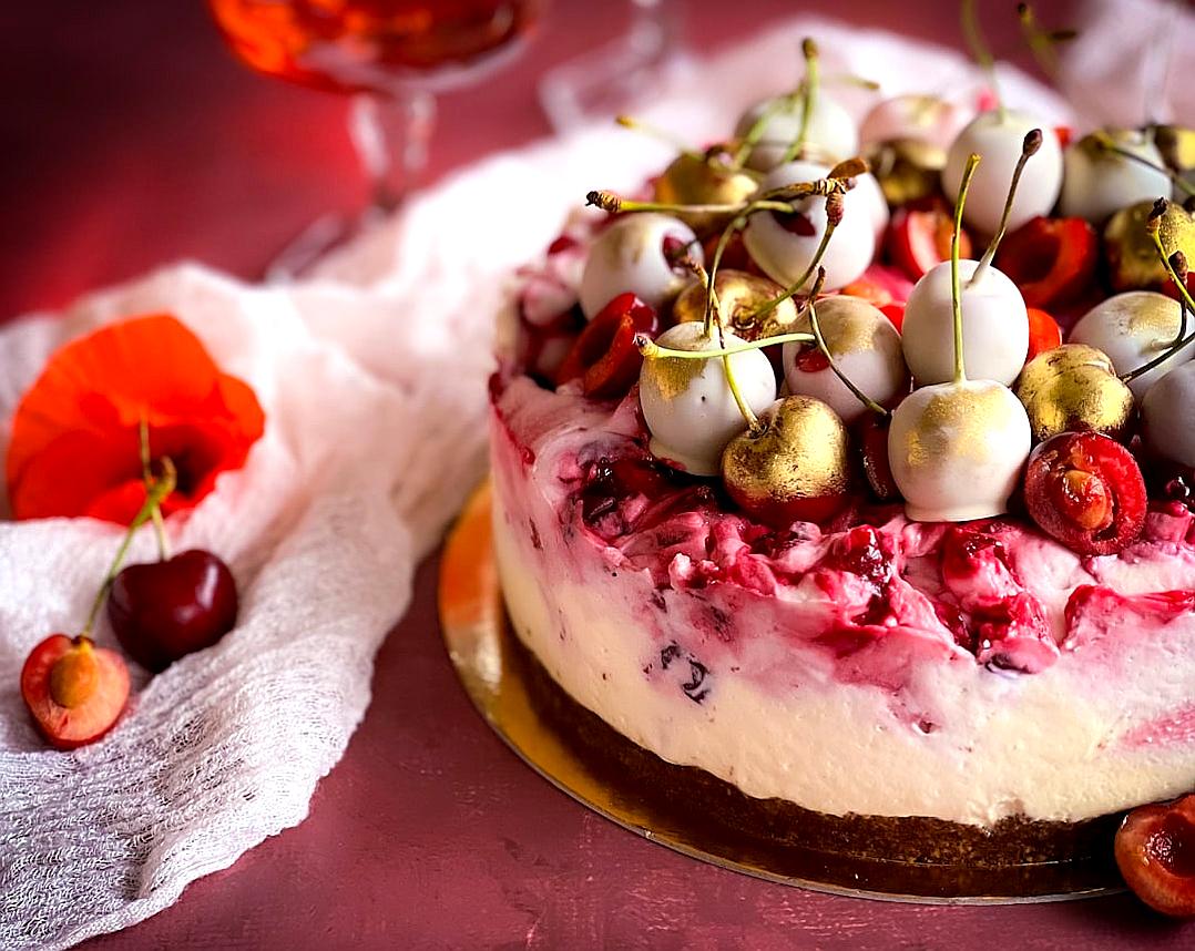 A delectable cherry and berry Cheesecake, topped with gold foil cherries, cherbelies, decorated on top of the cake. The background is pink, with an elegant touch that adds to its appeal. A beautiful white napkin sits beside it, adding to overall visual appeal. This photo was taken using Canon EOS R5 camera with Nikon NIKKOR Z macro 60mm f/28 lens, capturing every detail in stunning clarity and depth.