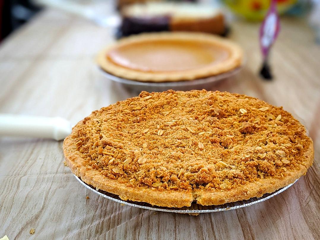 A photo of an apple pie with brown sugar crumble on top, sitting next to the cut pumpkin pie at an American diner in the style of aladmini vaporwave, shot from above.