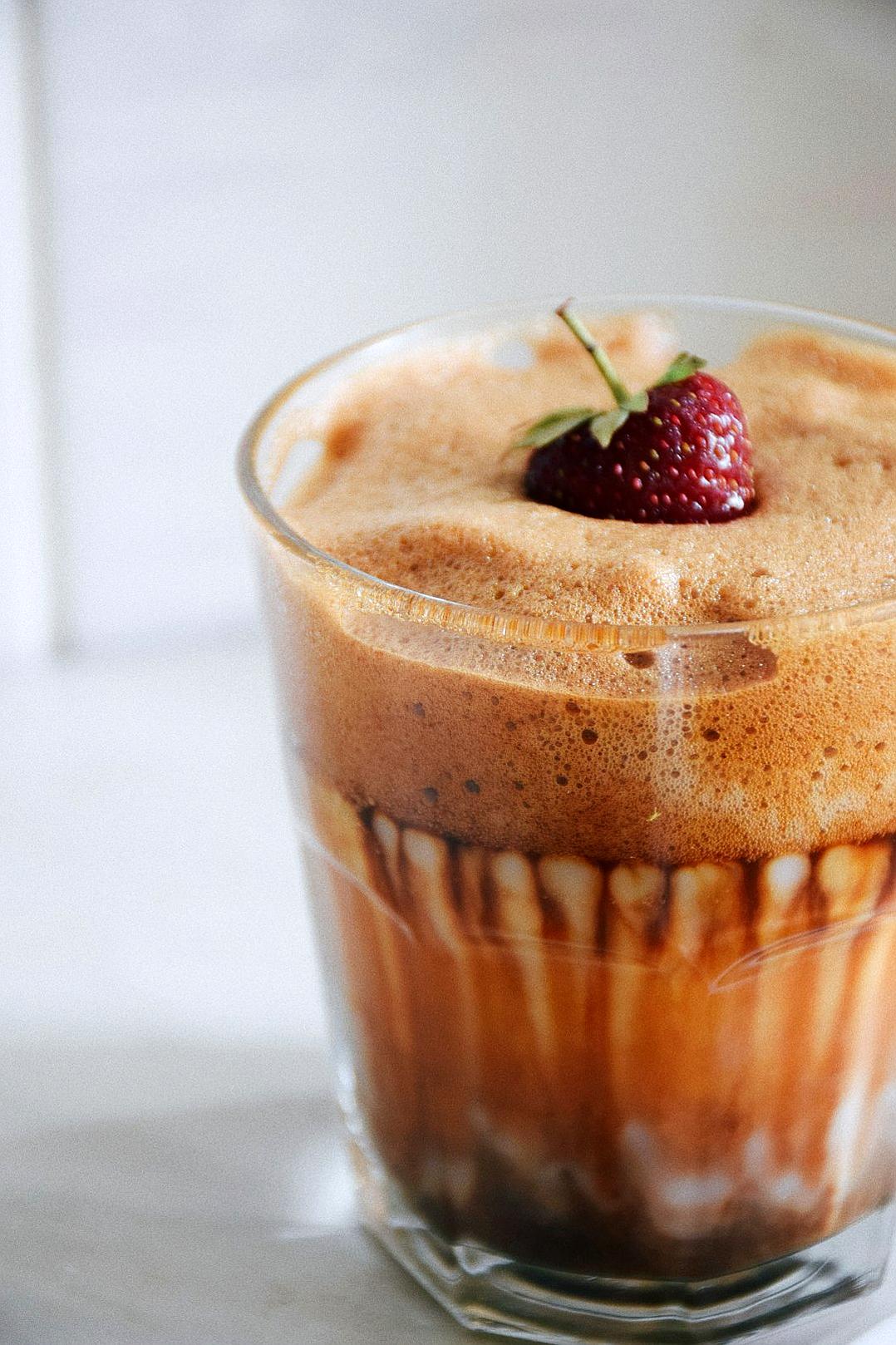 food photography, close up of thick coffee in glass with brown foam and chocolate drizzle, single strawberry on top, white background,