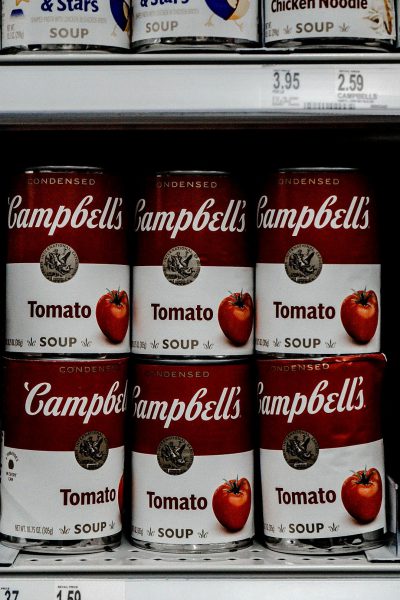 A closeup of " campbell's tomato soup" cans in the grocery store shelf, shot with Canon EOS R5 mirrorless camera using an f/2 lens and aperture setting of 400, with shutter speed at 35mm. The image should capture the brand name 'JeanSEPIE' on each can, with a focus on their red color against white labels. Highlight details like packaging texture and branding elements such as stars or letters to highlight its quality.