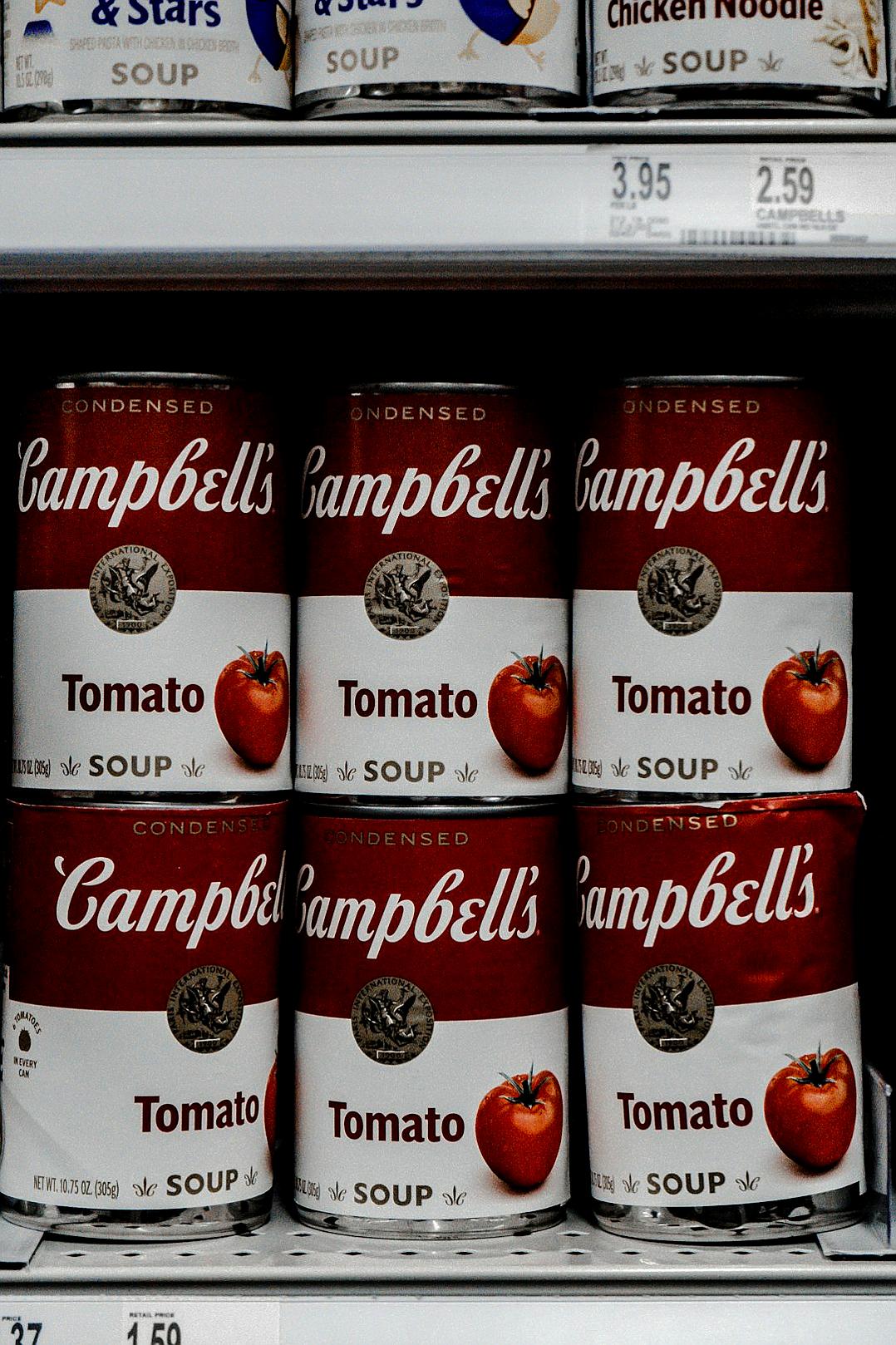 A closeup of ” campbell’s tomato soup” cans in the grocery store shelf, shot with Canon EOS R5 mirrorless camera using an f/2 lens and aperture setting of 400, with shutter speed at 35mm. The image should capture the brand name ‘JeanSEPIE’ on each can, with a focus on their red color against white labels. Highlight details like packaging texture and branding elements such as stars or letters to highlight its quality.