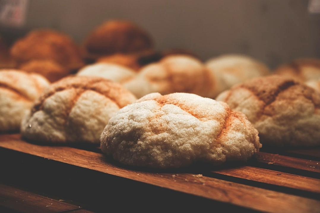 A close-up shot of freshly baked sourdough bread rolls on display at the bakery, highlighting their golden brown crust and delicious texture. The background is blurred to emphasize these fresh buns, creating an attractive visual. The image has a quaint simplicity, with light and dark amber tones, soft lighting, warm colors, and rich details in the style of [Rembrandt](https://goo.gl/search?artist%20Rembrandt).