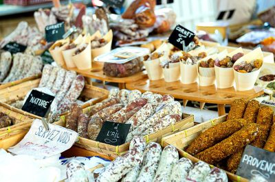 A market stall with various sausages from the provence, black signs written "hamster", and white paper bags of salami in plastic containers on wooden platters at an outdoor farmer's fair in Prov المشاركة" style raw taken by canon eos r5