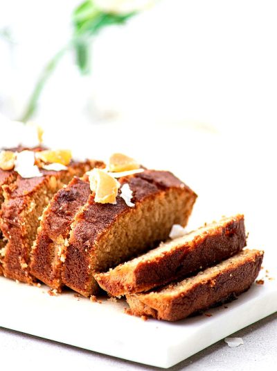 Close-up photo of sliced gingerbread loaf cake with coconut and honey, on a white marble platter against a white background with soft natural light. The cake was decorated in the style of C follower's Z and looks delicious and clean in a minimalistic, macro shot style befitting professional food photography.