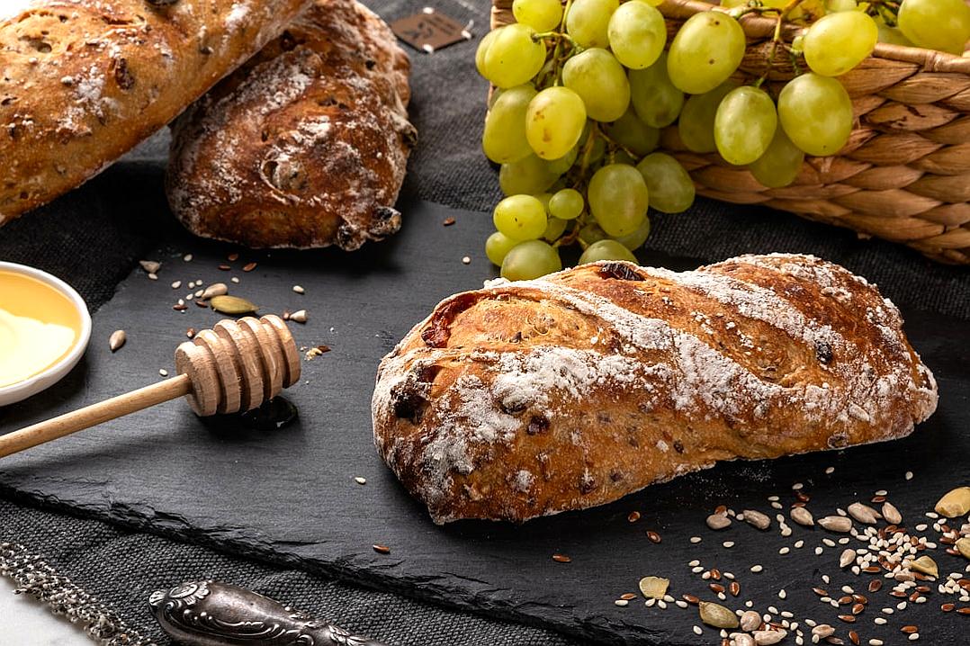 Savory French bread with grapes, honey and sunflower seeds on a black slate board. Food photography in the style of sunflower seeds.