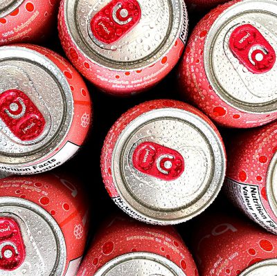 A pile of red and white soda cans with the logo "N SES organisations" on them, in an overhead shot from close up, with water droplets, in a high resolution style, for product photography.