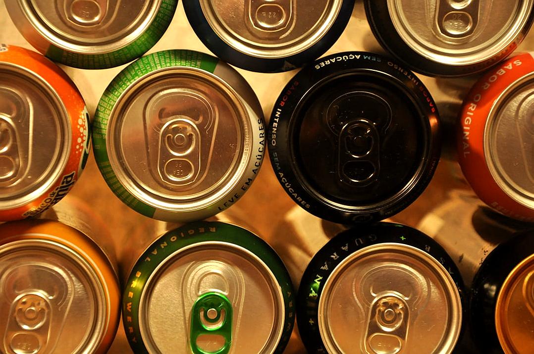 A closeup view of the tops of several cans, with green and orange labels. The cans have different colors such as black, white or silver. They all feature aluminum material and have circular shapes. From an overhead perspective, they show their whole bodies. There is no background behind them. Each can has unique patterns that give it individuality. Soft light illuminates each drink can, creating a warm atmosphere. This photo was taken using a Canon EOS R5 camera, in the style of minimal editing of the original text.