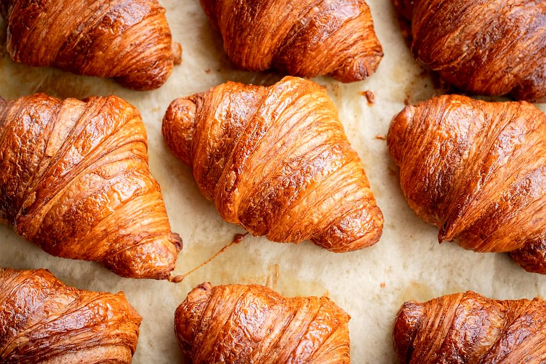 Top view of freshly baked croissants on parchment paper, food photography. Delicious and appetizing texture in the style of professional lighting. Soft shadows, no contrast in the style of professional color grading. Clean sharp focus, minimalistic, stock photo quality.